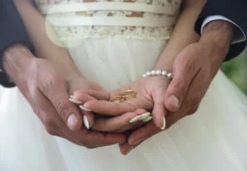 Mains réunies devant une robe de mariée blanche.