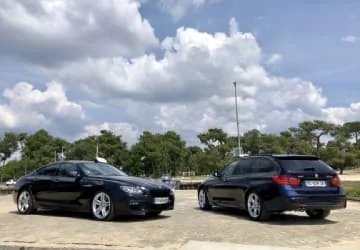 Deux berlines noires stationnées sur un parking sous un ciel nuageux.